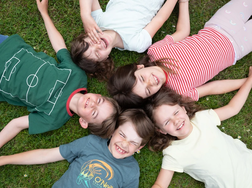 Kinder liegen auf einer Wiese im Kreis