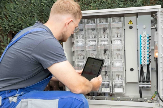 Mitarbeiter mit Netzplan vor einem Verteilerkasten 