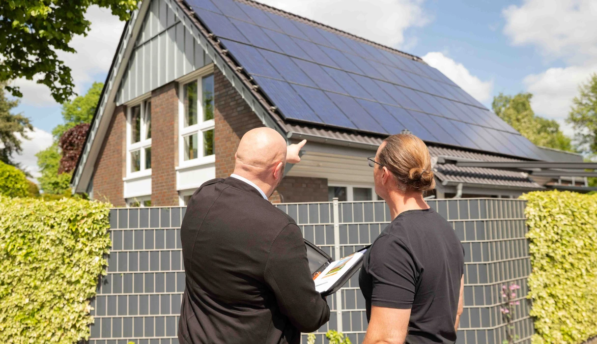 Beratungsgespräch vor einem Dach mit Solar-PV Modulen 