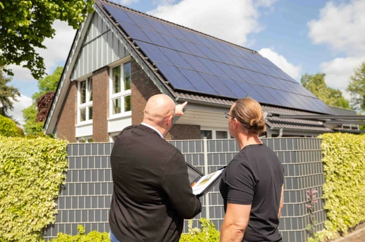 Beratungsgespräch vor einem Dach mit Solar-PV Modulen 