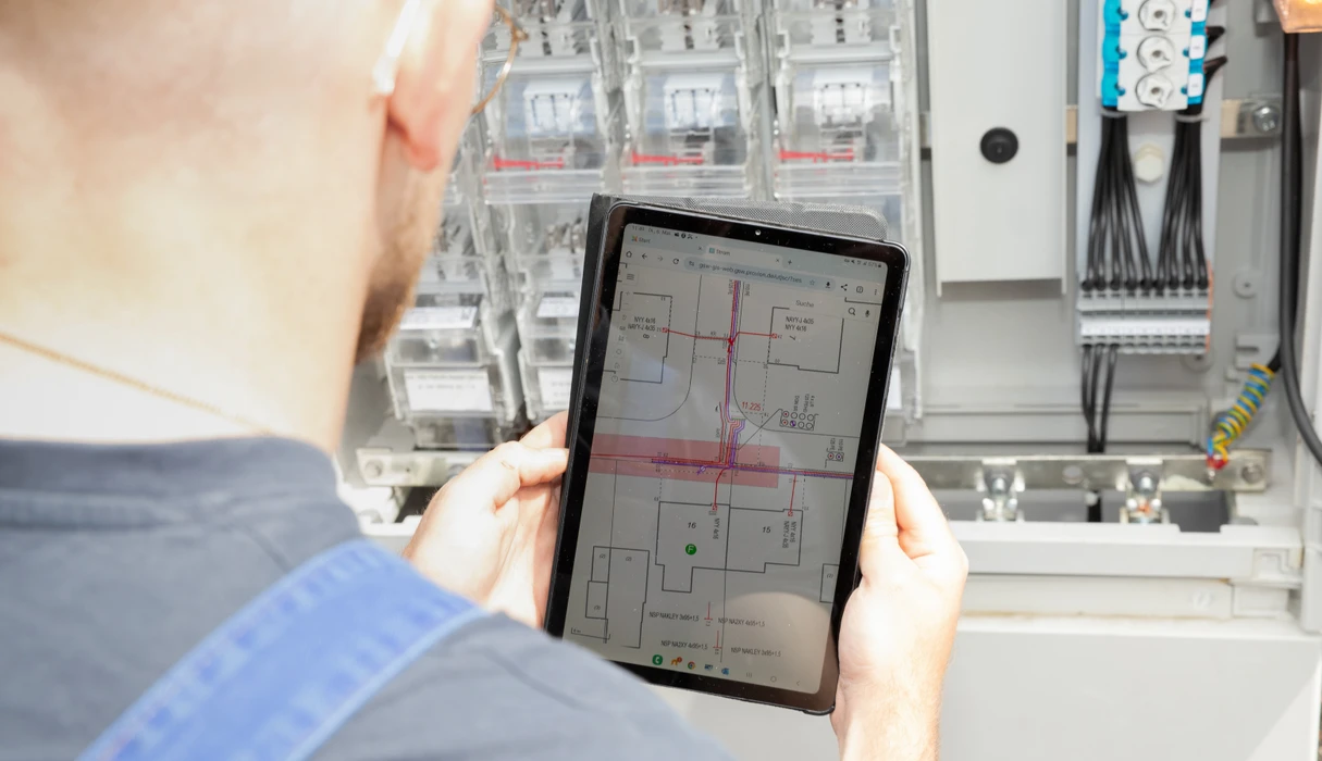 Tablet mit Netzplan vor Stromverteilerkasten