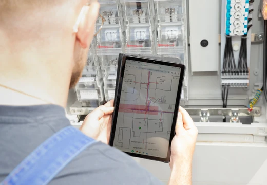 Tablet mit Netzplan vor Stromverteilerkasten