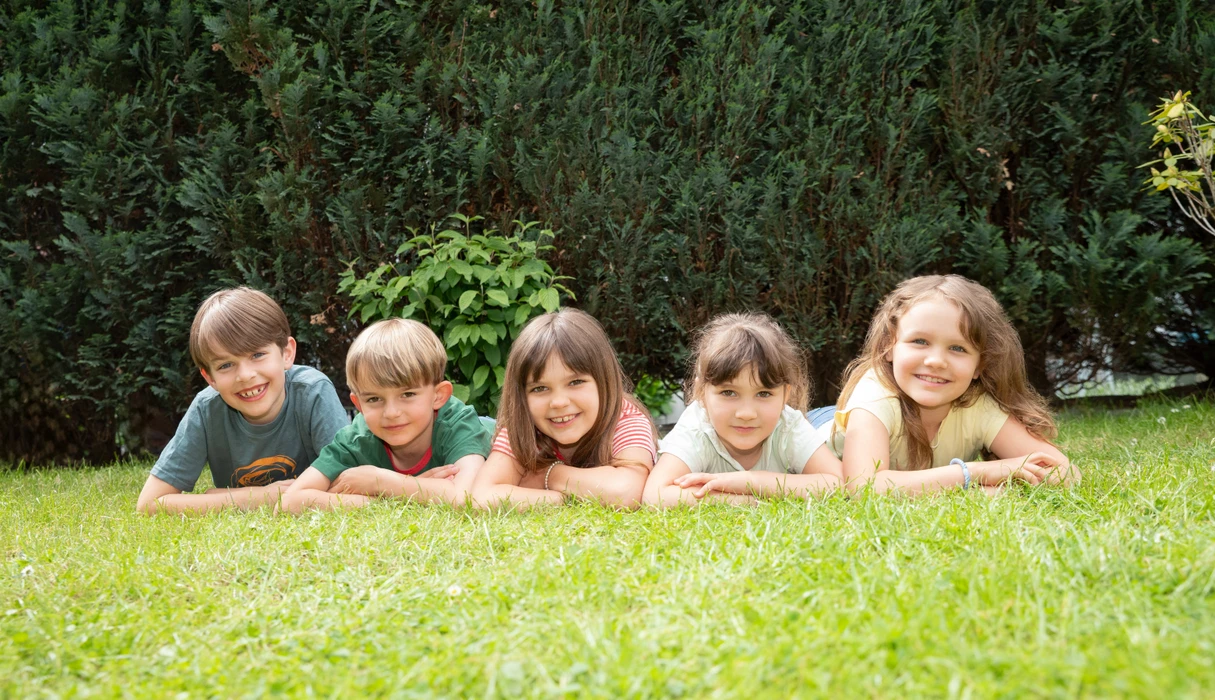 Imagebild: Kinder liegen auf einer Wiese und lächeln 