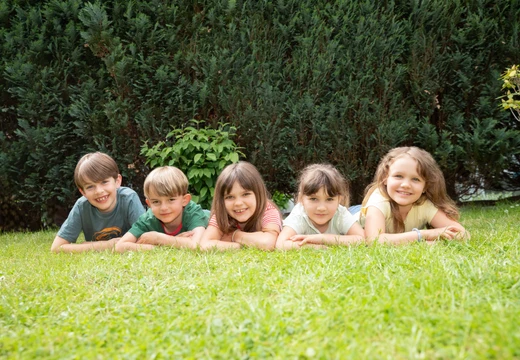Imagebild: Kinder liegen auf einer Wiese und lächeln 