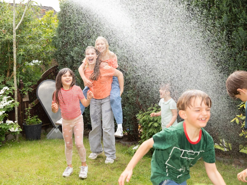 Kinder spielen im Garten mit einem Wasserschlauch