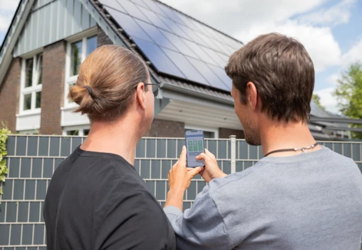 Zwei Männer stehen vor einem Haus und schauen auf einem Handy nach den Werten der Solaranlage